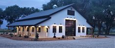 a white barn with black roof and lights on the front door is lit up at night