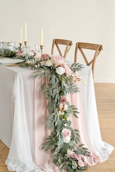 the table is set with pink and white flowers, greenery and candles on it