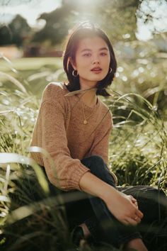 a woman sitting in tall grass with her legs crossed and looking off to the side