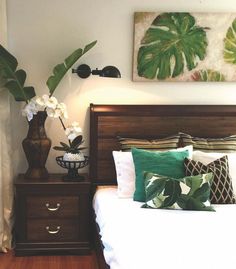 a bed with white and green pillows on top of it next to a wooden night stand