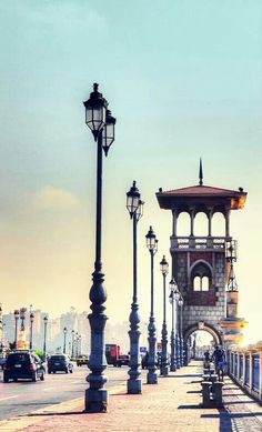 an old clock tower sitting on the side of a road next to some street lamps