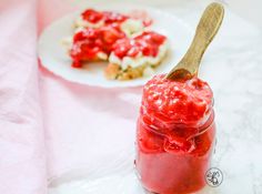 a jar of strawberry jam next to a plate of food on a pink table cloth