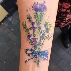 a tattoo on the leg of a woman that has flowers and a ribbon around it