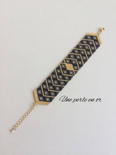 a black and gold bracelet with a chain attached to the clasp, on a white background