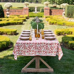 an outdoor table set up with plates and glasses on it in the middle of a garden