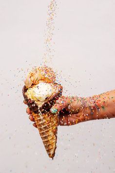 an ice cream cone with sprinkles being held by someone's hand