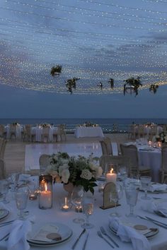 an outdoor dining area with white linens and lights strung from the ceiling above it