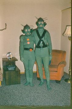 two people dressed as aliens standing next to each other in front of a couch and chair