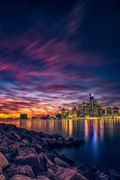 the city skyline is lit up at night with colorful clouds and bright lights in the sky