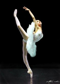 a ballerina in white tutu and feathered skirt doing a ballet move with her arms stretched out