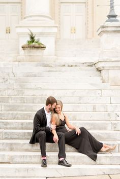 a man and woman sitting on the steps in front of a building, hugging each other