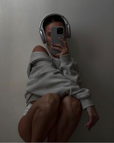 a woman wearing headphones is sitting on the floor and taking a selfie with her cell phone