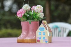 a pink boot with flowers in it sitting next to a small house shaped planter