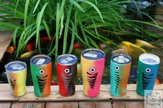 five colorful cups with eyes and fish on them are lined up in front of a pond