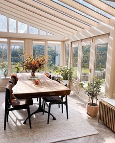 a dining room table and chairs in front of large windows with potted plants on them