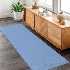 a blue rug is on the floor next to a wooden dresser and potted plant