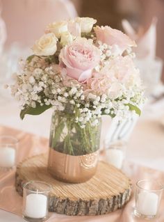 a vase filled with pink and white flowers on top of a wooden table next to candles