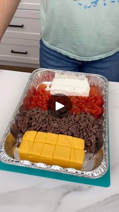 a person standing in front of a tray with food on it and cheese, tomatoes, peppers, and other foods