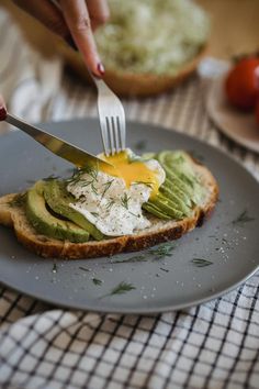 a person cutting an egg on top of toast with avocado and sour cream