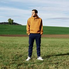 a man standing in the middle of a field wearing an orange sweatshirt and blue sweatpants