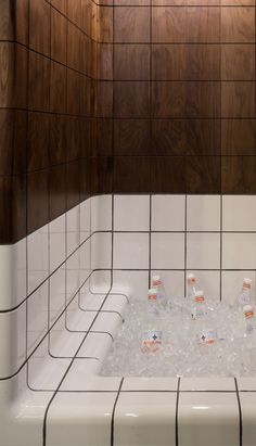 a bathtub filled with lots of ice and bottles of water next to a tiled wall