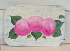 a painting of three pink roses with green leaves on a white painted wood paneled wall