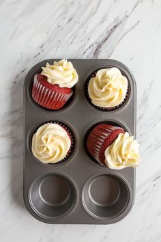 four cupcakes with white frosting in a muffin tin on a marble countertop