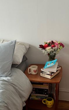 a table with books, coffee mug and flowers on it in front of a white wall