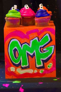 two cupcakes are sitting on top of an orange box with the word omg painted on it