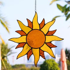 a stained glass sunflower hanging from a chain in front of some trees and buildings