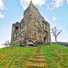 an old stone building sitting on top of a lush green hillside next to a tree