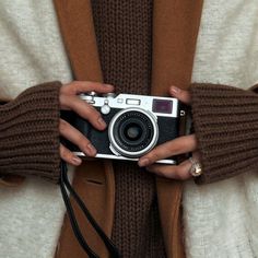 a woman holding an old camera in her hands while wearing brown sweaters and gloves