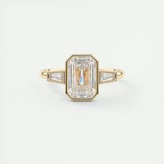 an emerald cut diamond ring with three baguets in yellow gold and white diamonds