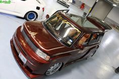 two cars parked in a garage next to each other and one is red with gold trim