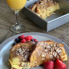 two pieces of french toast on a plate with berries and strawberries next to a glass of orange juice