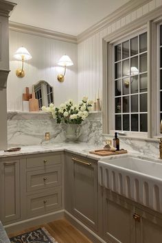 a white kitchen with marble counter tops and gold trim around the sink, along with two large windows