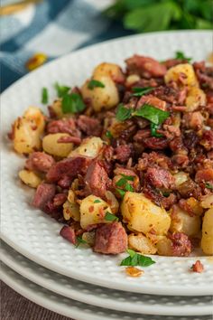 a white plate topped with potatoes covered in meat and garnished with parsley