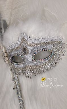 Obatala inspired mask with rhinestone trim, crystals, and cowrie shells on a dazzling bling stick. ✨️𝕆ℝ𝕀𝕊ℍ𝔸 𝓲𝓷𝓼𝓹𝓲𝓻𝓮𝓭 Ａｒｔ, glam luxury ᴄᴜꜱᴛᴏᴍ ᴘɪᴇᴄᴇꜱ, ɴᴏᴠᴇʟᴛɪᴇꜱ & ᴍᴏʀᴇ✨️🕊🗿🧜🏾‍♀️⚡️🍯🌪🌈🌋🧲🗡🛡🎭🐚🔥 Each item is respectfully made with the highest quality materials. Please note: All items are made to order and ship within 4-6 weeks! Style may vary slightly due to material ... Silver Rhinestone Eye Mask For Masquerade, Silver Rhinestone Eye Masquerade Mask, Silver Masquerade Mask With Rhinestones For Costume Party, Silver Rhinestone Masquerade Mask For Costume Party, Rhinestone Masquerade Mask For Mardi Gras Carnival, Carnival Rhinestone Eye Mask, Carnival Eye Mask With Rhinestones, Mardi Gras Masquerade Mask With Rhinestones For Carnival, Silver Rhinestone Masquerade Mask For Carnival