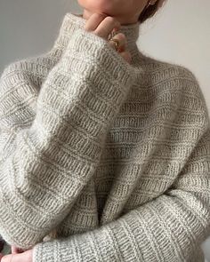 a woman is wearing a sweater and holding her hand under her chin as if she's looking at the camera