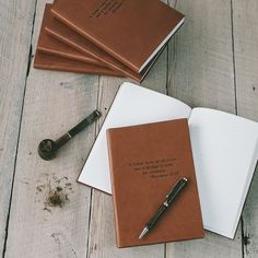 three brown notebooks and a pen on a wooden table