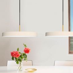 a vase with flowers sitting on top of a white table next to two hanging lights