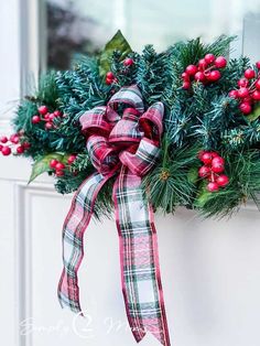 a christmas wreath with red berries and greenery hanging from the side of a door