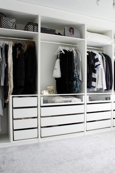 a white closet with drawers and clothes hanging on the walls, along with other items