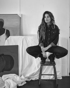 a woman sitting on top of a stool in front of paintings