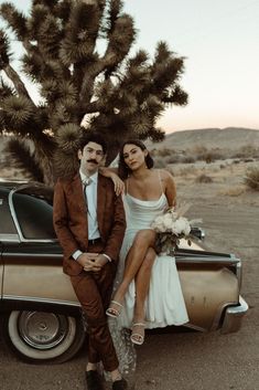 a man and woman sitting on the back of a car in front of a joshua tree