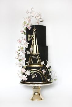 a three tiered black and gold cake with flowers on it's side, in the shape of the eiffel tower