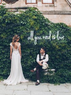 a bride and groom sitting on a bench in front of a wall with the words all you need is love