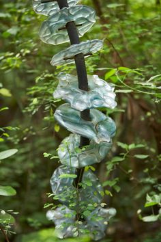 several pieces of glass hanging from a tree branch in the middle of some green leaves