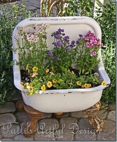 a tub filled with lots of flowers sitting on top of a stone floor next to plants