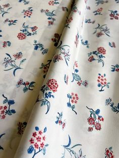 a white and blue floral print fabric with red flowers on the bottom half of it